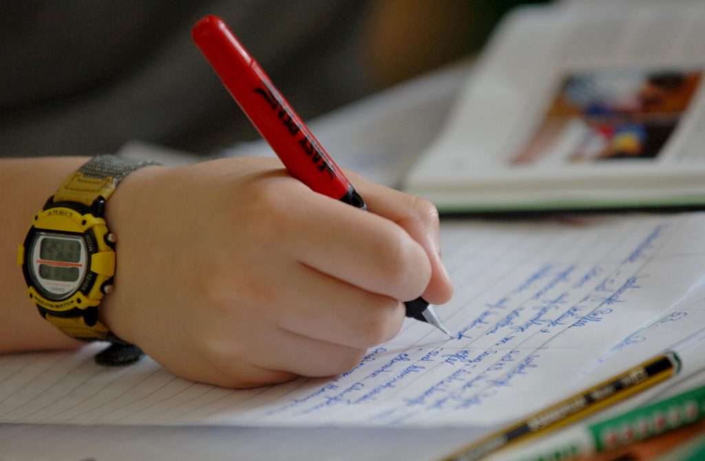 Hier sehen Sie wie ein Schüler einen Text schreibt. Es ist die Hand, der Stift sowie das Blatt Papier zu sehen.